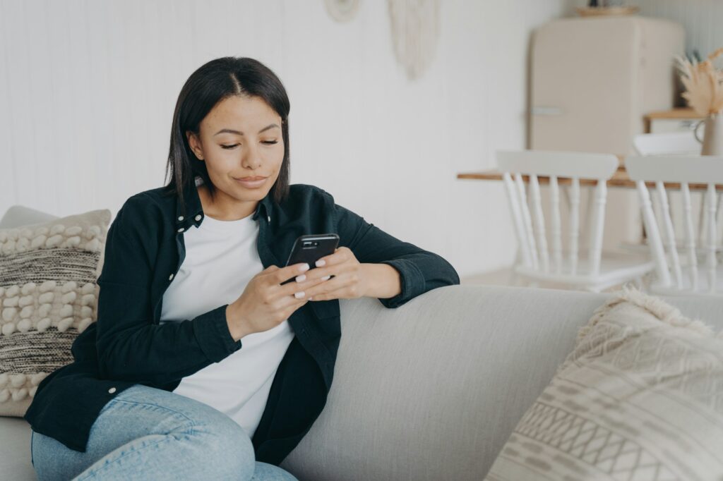 Female uses mobile apps holding smartphone, chatting in social networks, shopping online at home